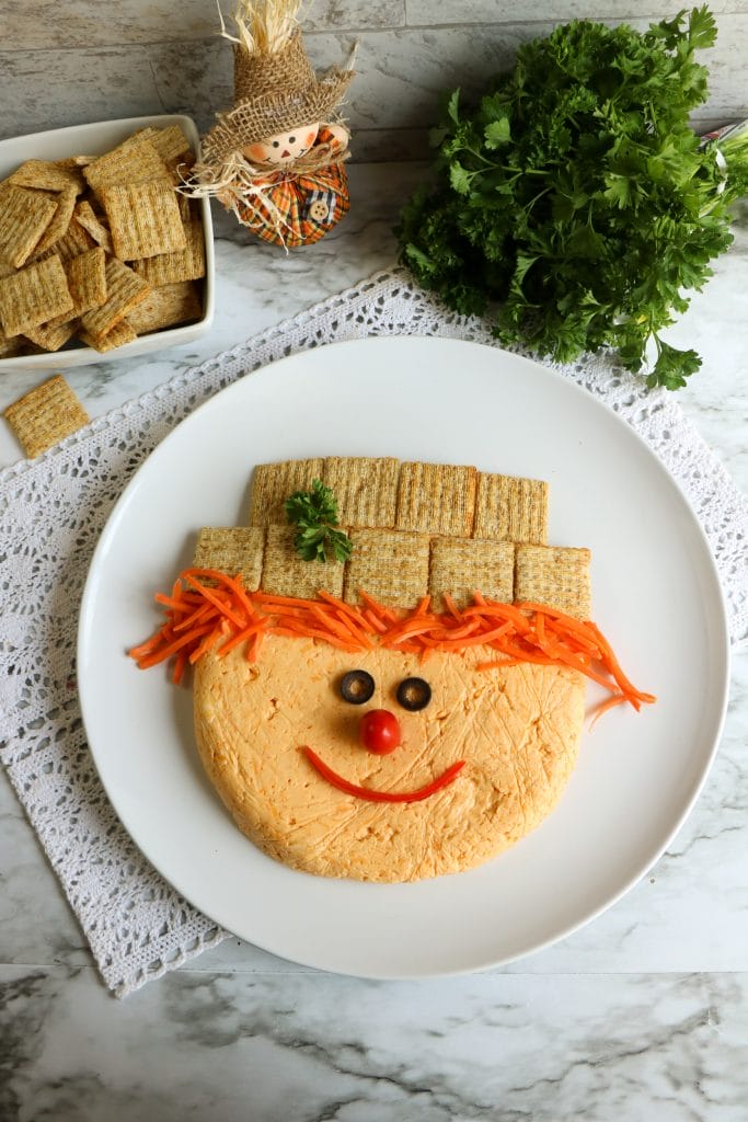 I have the perfect, easy fall appetizer for your today. This fun and delicious fall cheeseball recipe is a great idea as a snack or party food and a healthier treat for Halloween.  Make this adorable scarecrow cheeseball with a combination of three cheeses, shredded carrot, herbs and a just few additional ingredients. 
