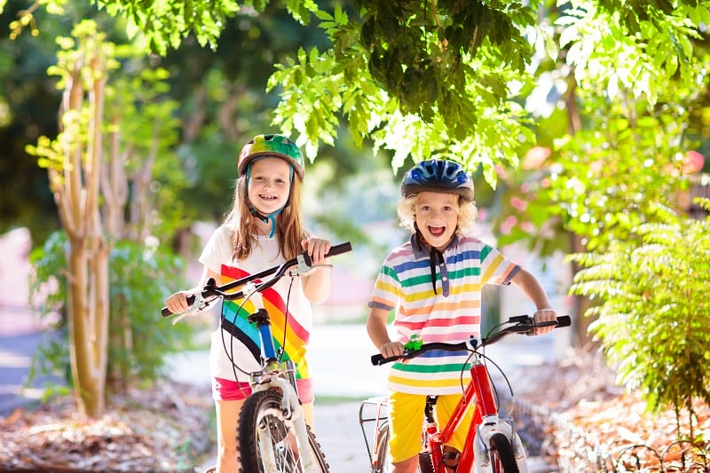 Kids on bike in park. Children going to school wearing safe bicycle helmets. Little boy and girl biking on sunny summer day. Active healthy outdoor sport for young child. Fun activity for kid.