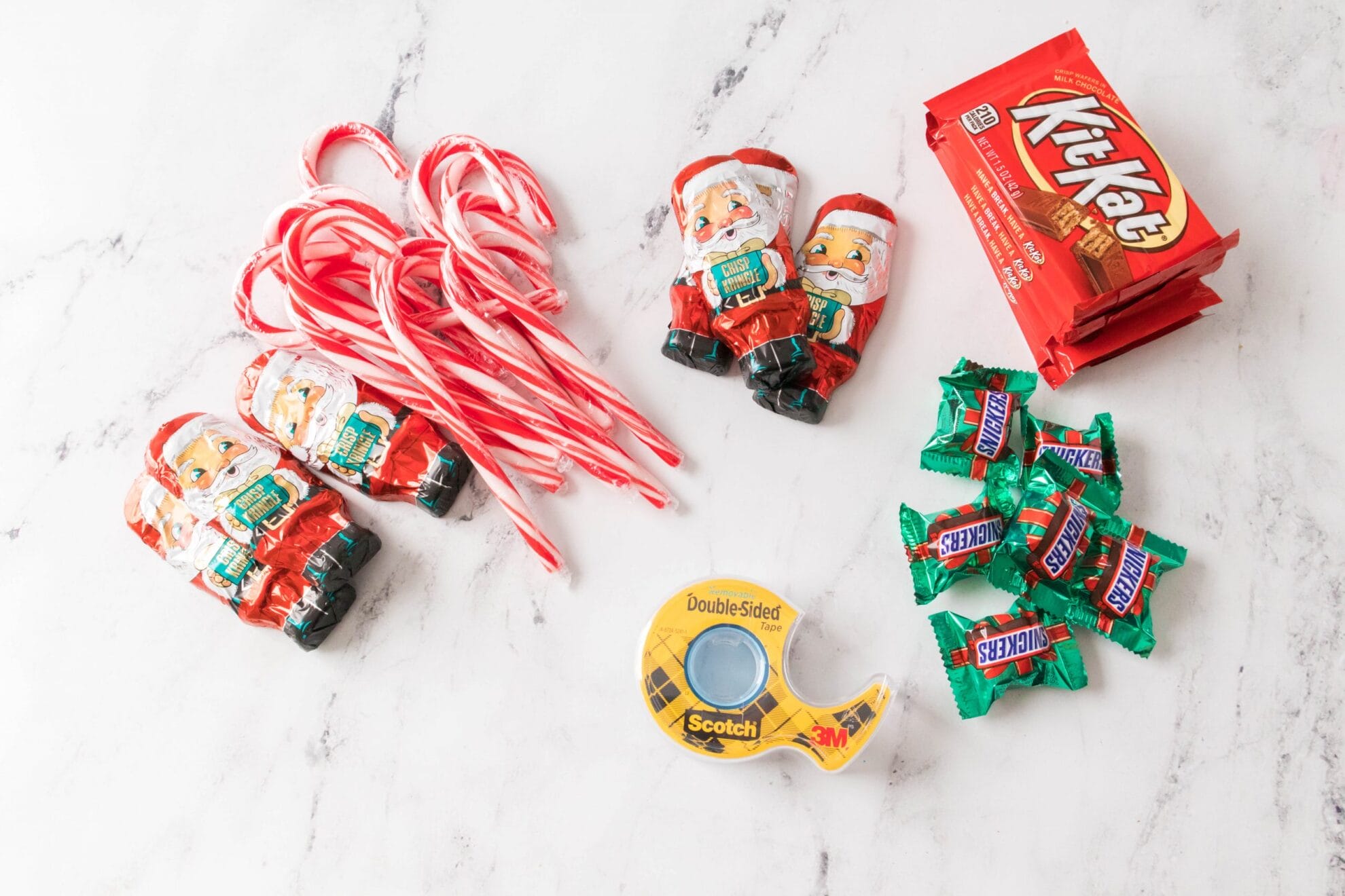 candy canes, chocolate santas, double sided tape, snickers and kit kats on marble surface