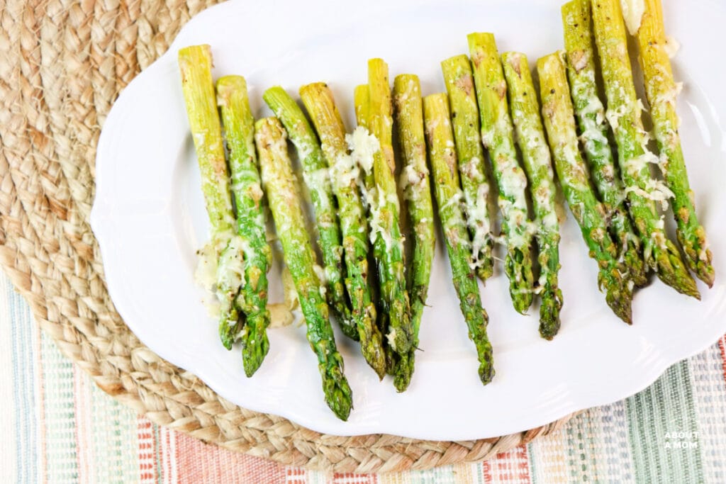 white platter with baked asparagus covered in cheese